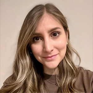 Primo piano di giovane donna, capelli lunghi e biondi, sorride con uno sguardo dolce.